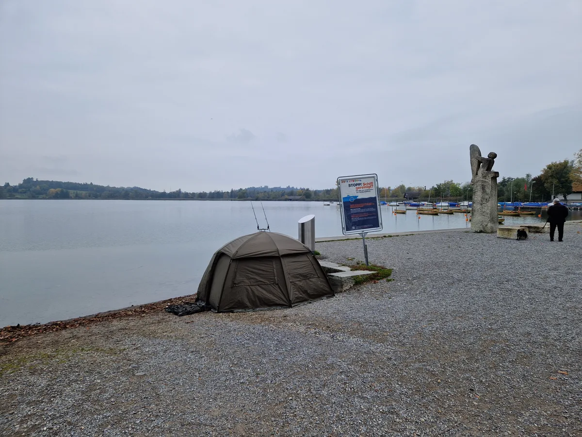 Ein kleines, olivgrünes Zelt steht am Seequai in Pfäffikon. Man sieht zwei Angeln, die vor dem Zelt an der Quaimauer befestigt sind.